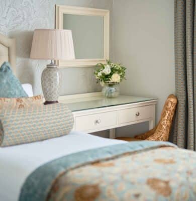 Elegant hotel room with plush bed, luxurious pillows, classic decor, stylish desk, fresh flowers, and natural light.