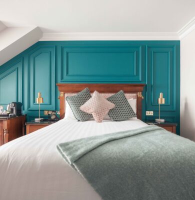 Elegant hotel room with plush bedding, teal feature wall, and modern amenities, offering a welcoming atmosphere.