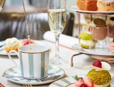 Elegant afternoon tea setup with striped china, pouring teapot, pastries, and champagne. Luxurious hotel dining experience.