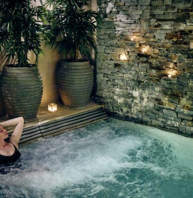 Relax in a serene indoor hot tub surrounded by stone walls and lush plants at our luxury hotel spa. Perfect for relaxation.
