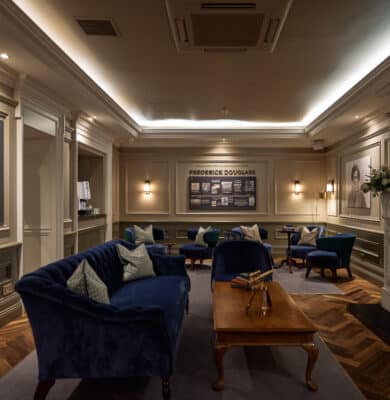 Cosy lounge with elegant blue sofas, framed art, warm lighting, and a luxurious fireplace; perfect for relaxation.