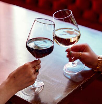 Guests enjoy a toast with red and white wine in a stylish hotel lounge with elegant red seating, perfect for relaxation and celebration.