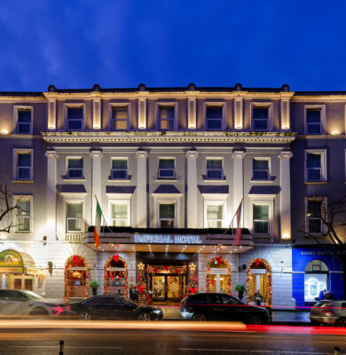 Elegant hotel entrance illuminated at night with festive decor and vibrant atmosphere, ideal for your luxurious stay.