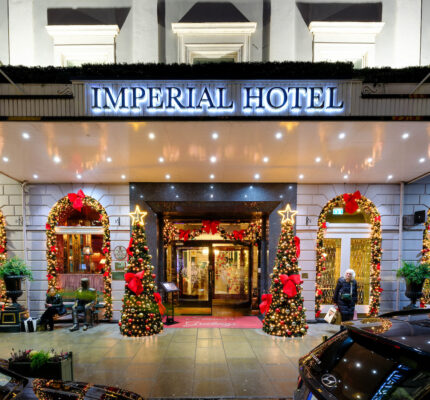 Festive hotel entrance adorned with Christmas lights, wreaths, and decorated trees, welcoming guests with holiday charm.