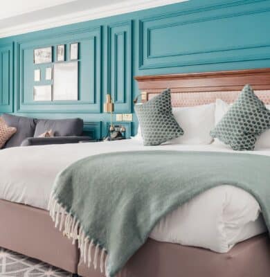 Elegant hotel room with plush king-size bed, stylish teal feature wall, cosy armchair, and soft lighting, promising comfort.