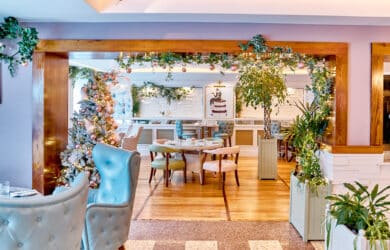 Cosy hotel dining area with elegant decor, festive garlands, lush plants, and plush seating, perfect for a delightful meal.