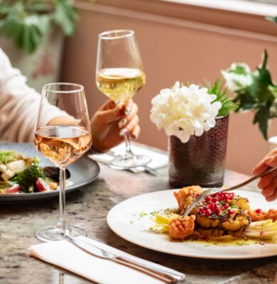 Elegant hotel dining with gourmet dishes, fine wine, fresh flowers, and serene atmosphere by a sunlit window.