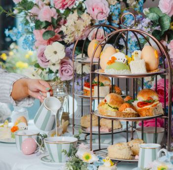 Elegant afternoon tea with tiered savouries, pastel flowers, and fine china in a luxurious hotel setting.